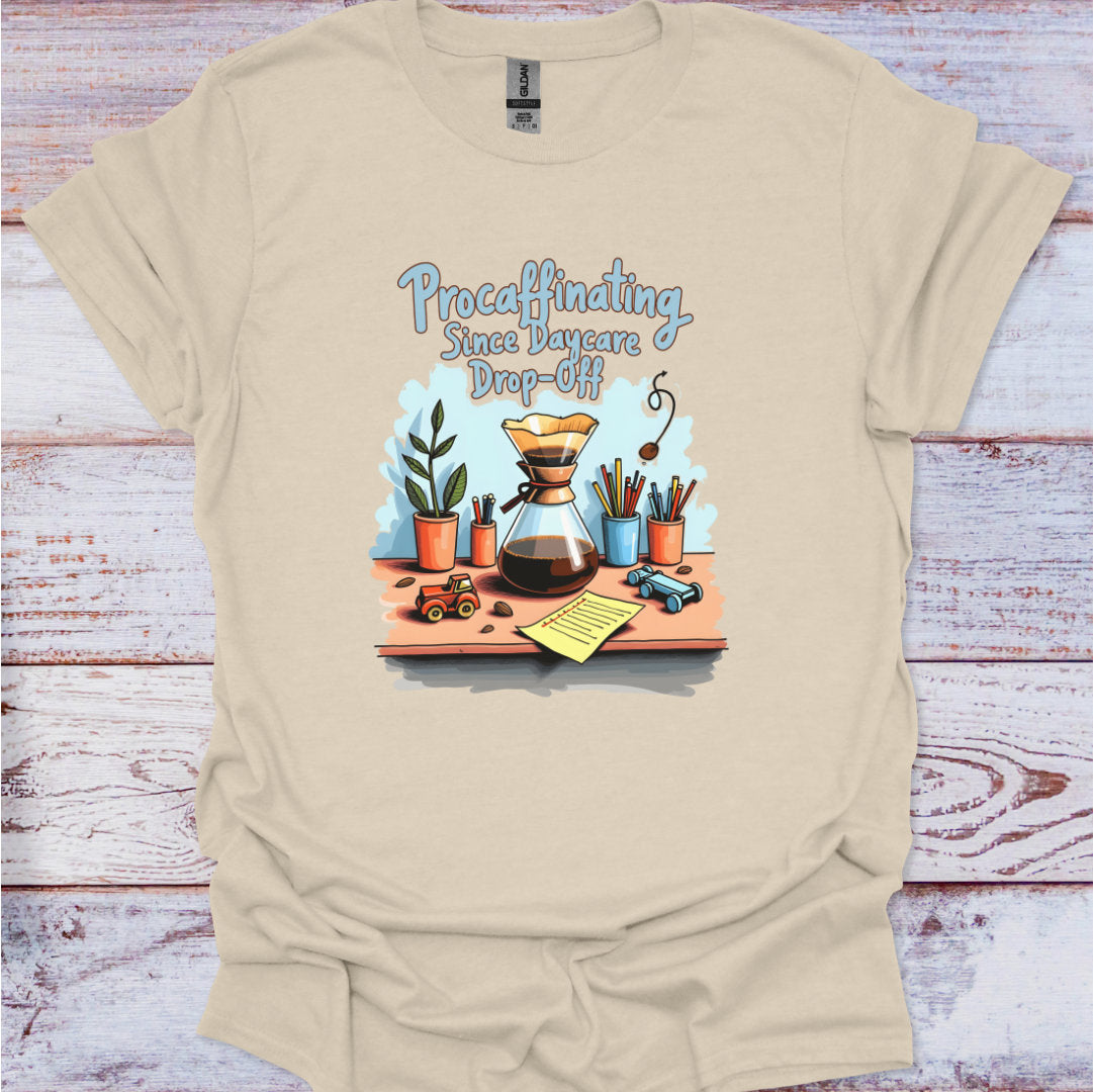 Beige t-shirt with a graphic design featuring a coffee maker, plants, and text on a wooden surface.