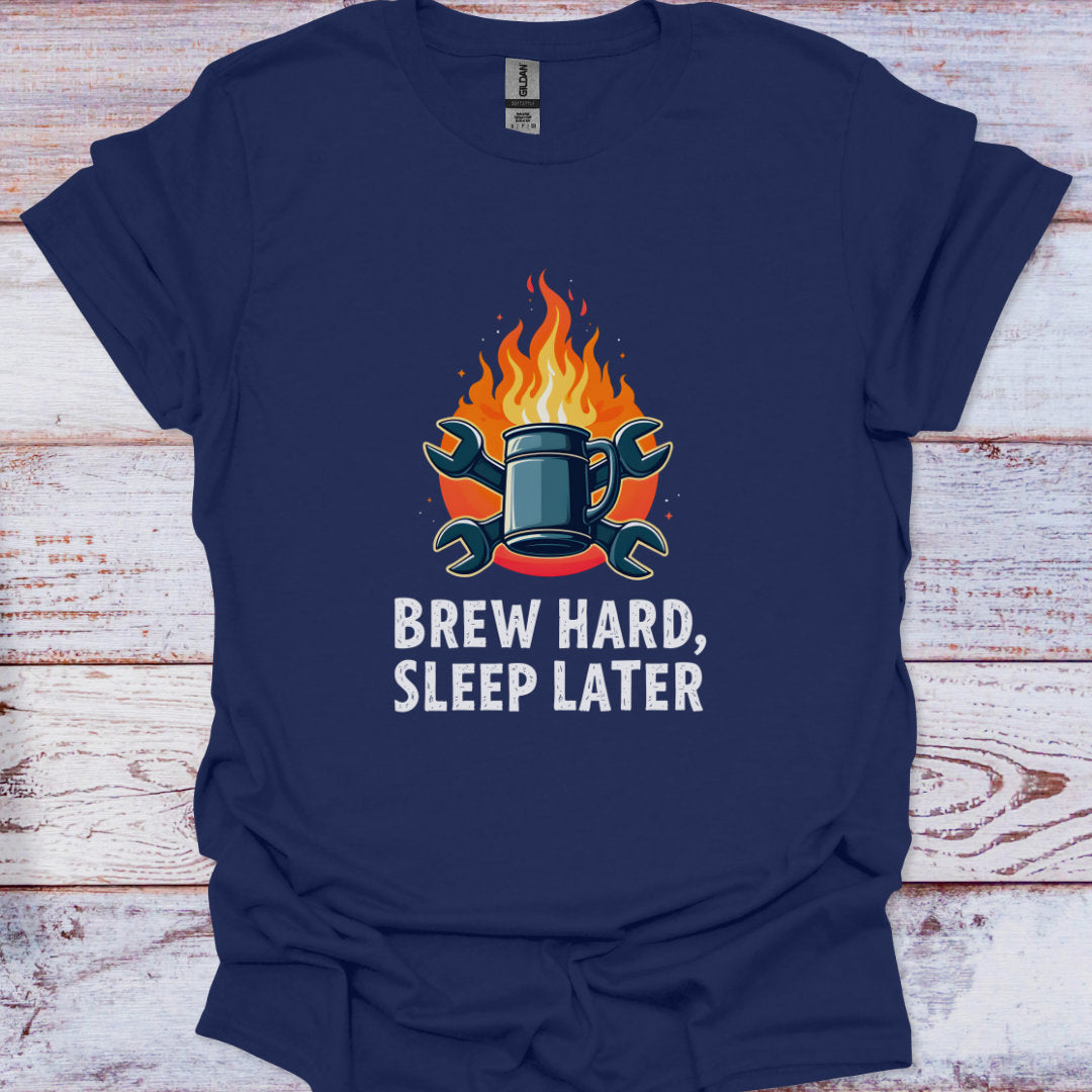 Navy blue t-shirt with a graphic of a mug and flames and text 'Brew Hard, Sleep Later' on a wooden surface.