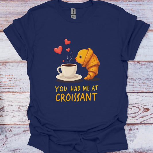 Navy blue t-shirt with a cartoon croissant and coffee cup graphic and text 'You Had Me at Croissant' on a wooden surface.