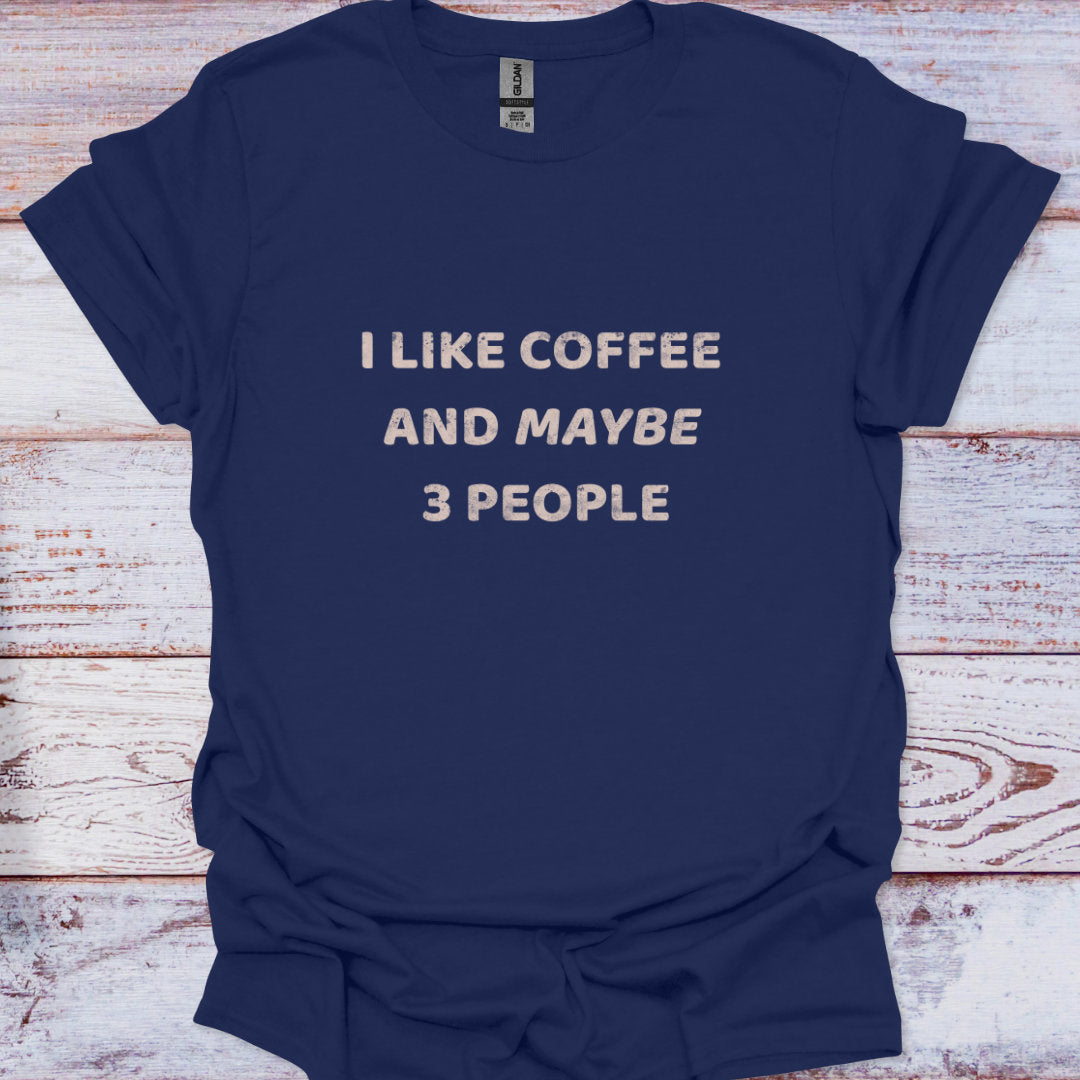 Navy blue t-shirt with white text 'I LIKE COFFEE AND MAYBE 3 PEOPLE' on a wooden surface