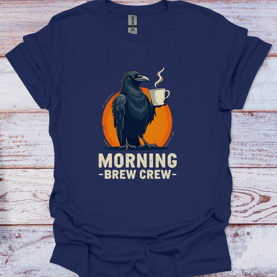 Navy blue t-shirt with a crow holding a coffee cup and 'Morning Brew Crew' text on an orange circle, against a wooden background.