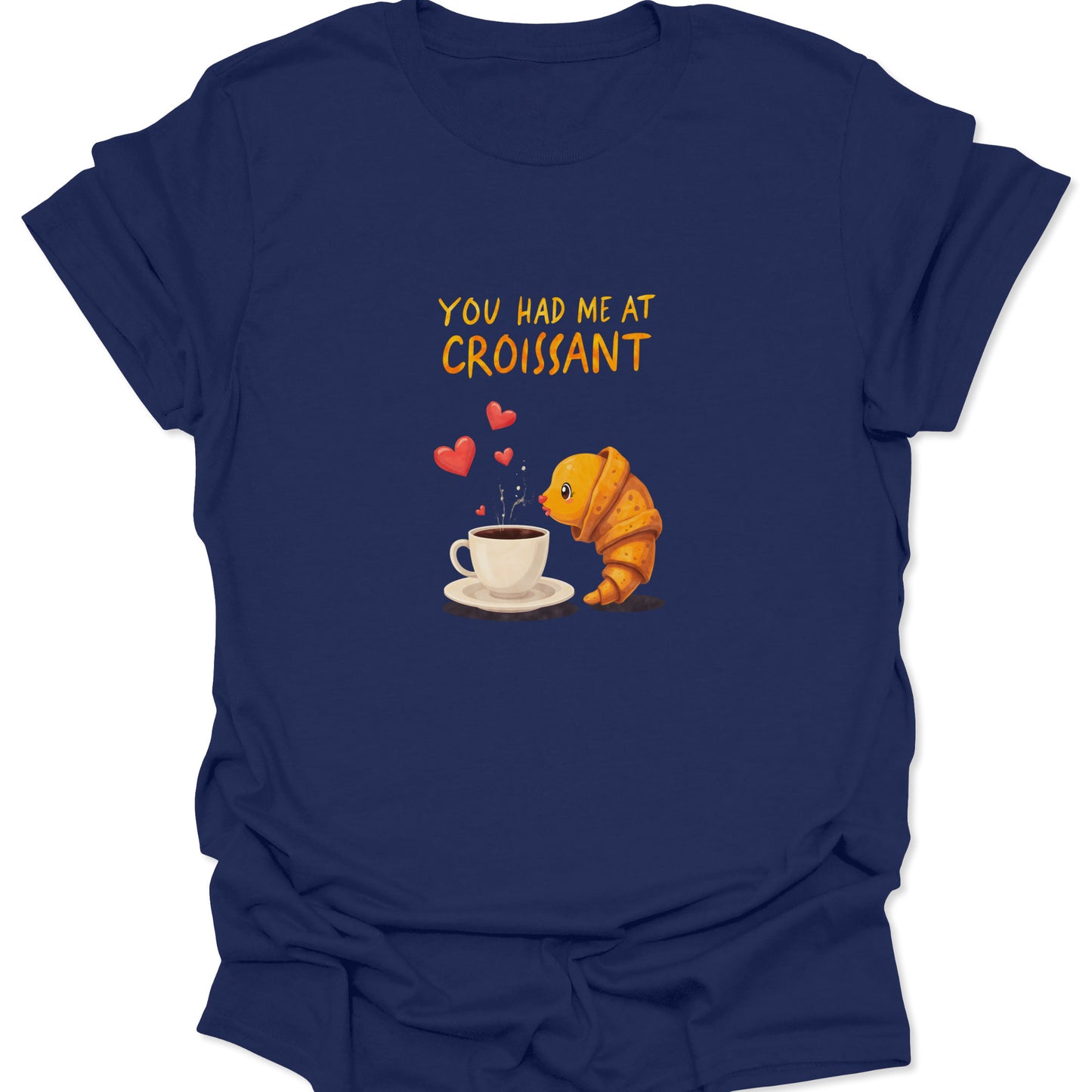 Navy blue graphic tee with warm-toned lettering and a croissant-and-coffee design. Visually communicates deep love for carbs and caffeine with floating heart icons.