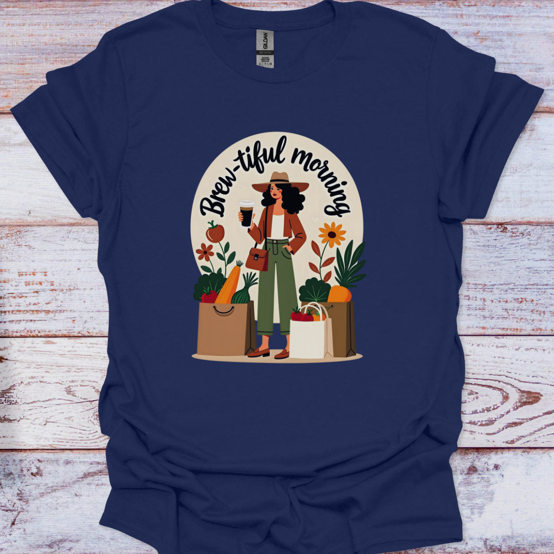 Navy blue t-shirt with a graphic of a woman holding a coffee cup and shopping bags, with 'Brew-iful morning' text, on a wooden surface.