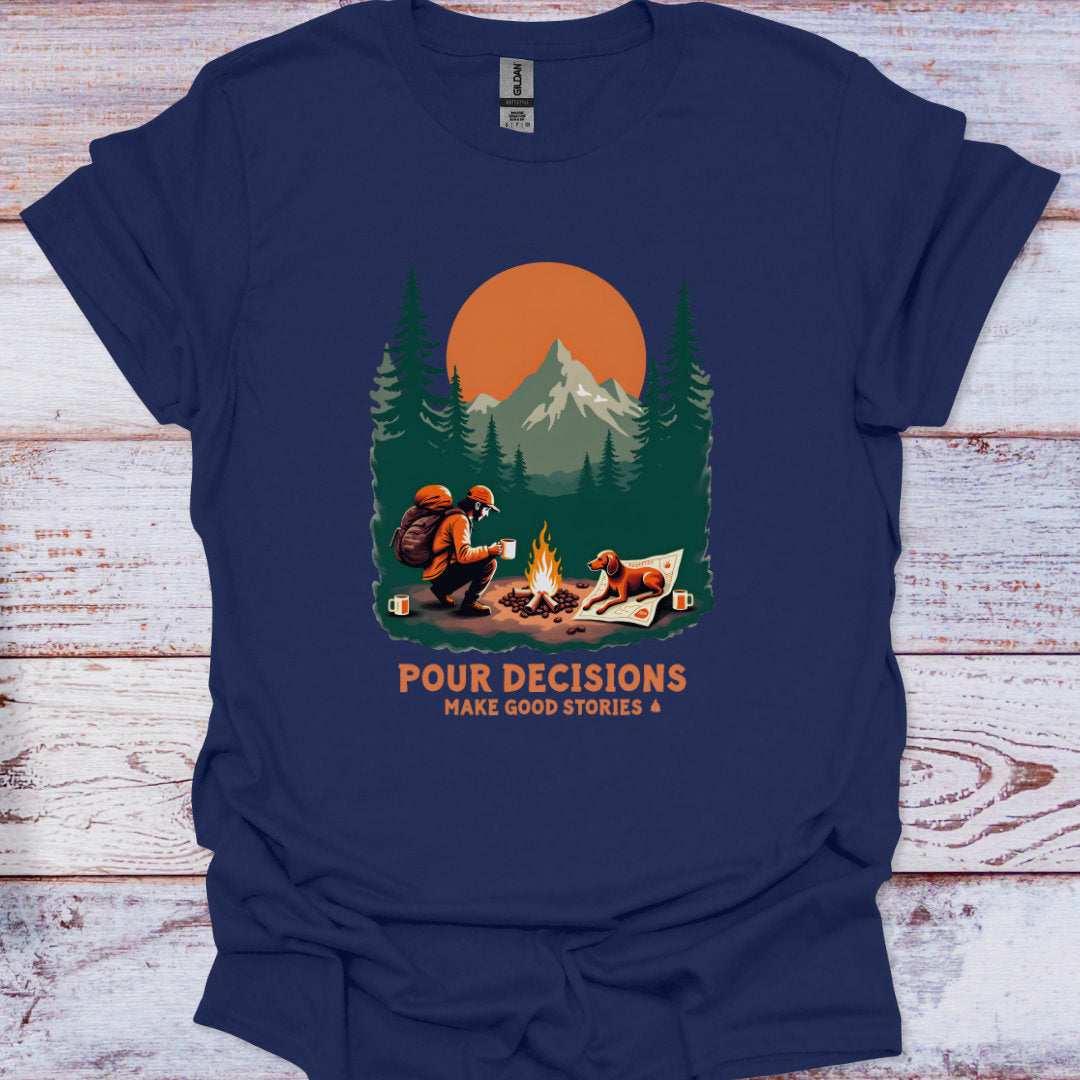 Navy blue t-shirt with a graphic of a man and his dog  by a campfire and mountains, with text 'Pour Decisions Make Good Stories &', on a wooden surface.