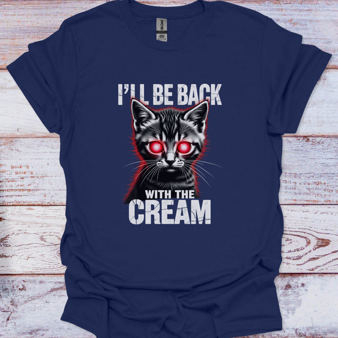 Navy blue t-shirt with a graphic of a cat with red eyes and text 'I'll be back with the cream' on a wooden surface.