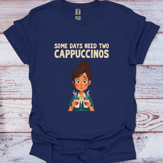 Navy blue t-shirt with cartoon character and text 'Some days need two Cappuccinos' on a wooden surface.