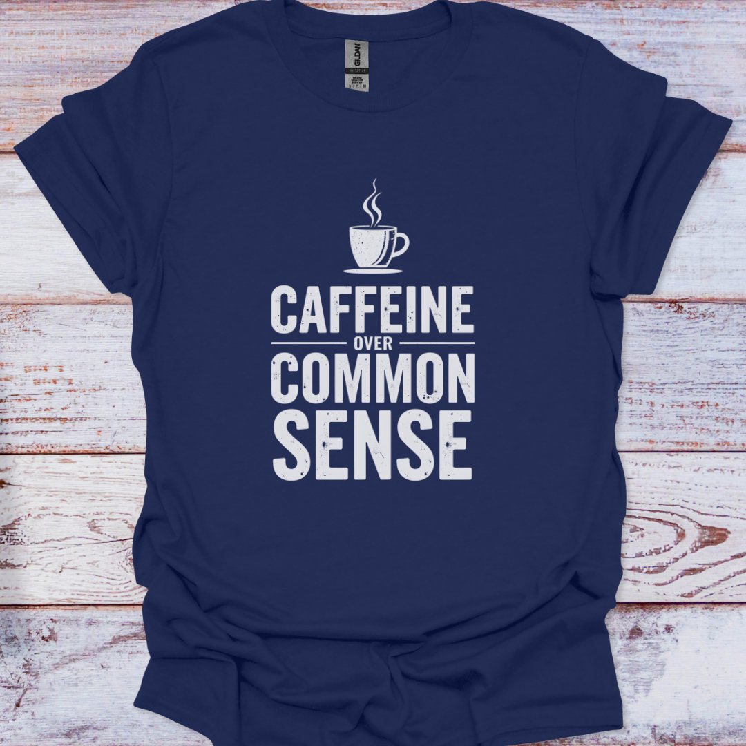 Navy blue t-shirt with white text 'CAFFEINE OVER COMMON SENSE' and a coffee cup graphic on a wooden surface.