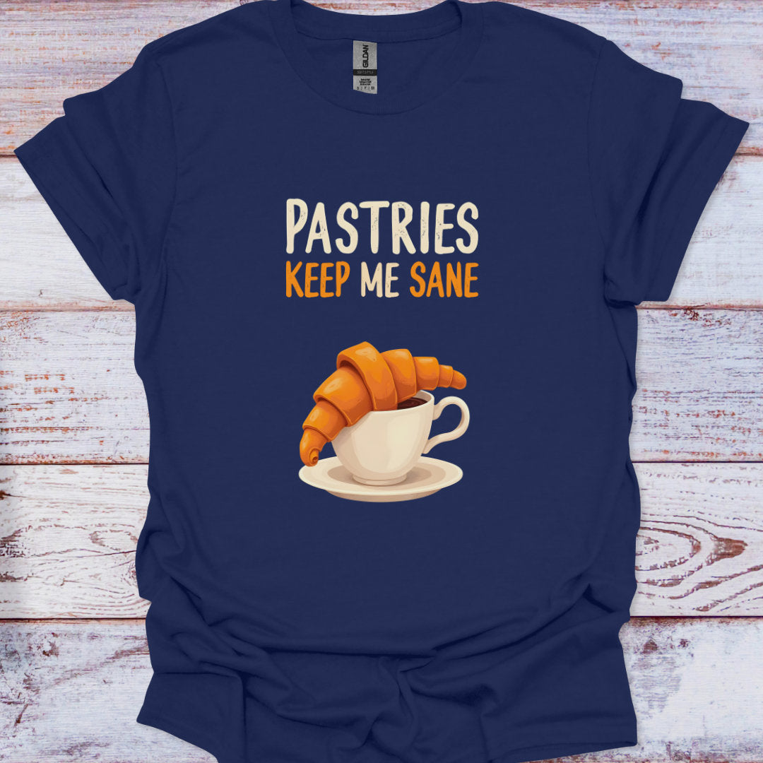 Navy blue t-shirt with a graphic of a croissant and coffee cup and text 'Pastries Keep Me Sane' on a wooden surface.