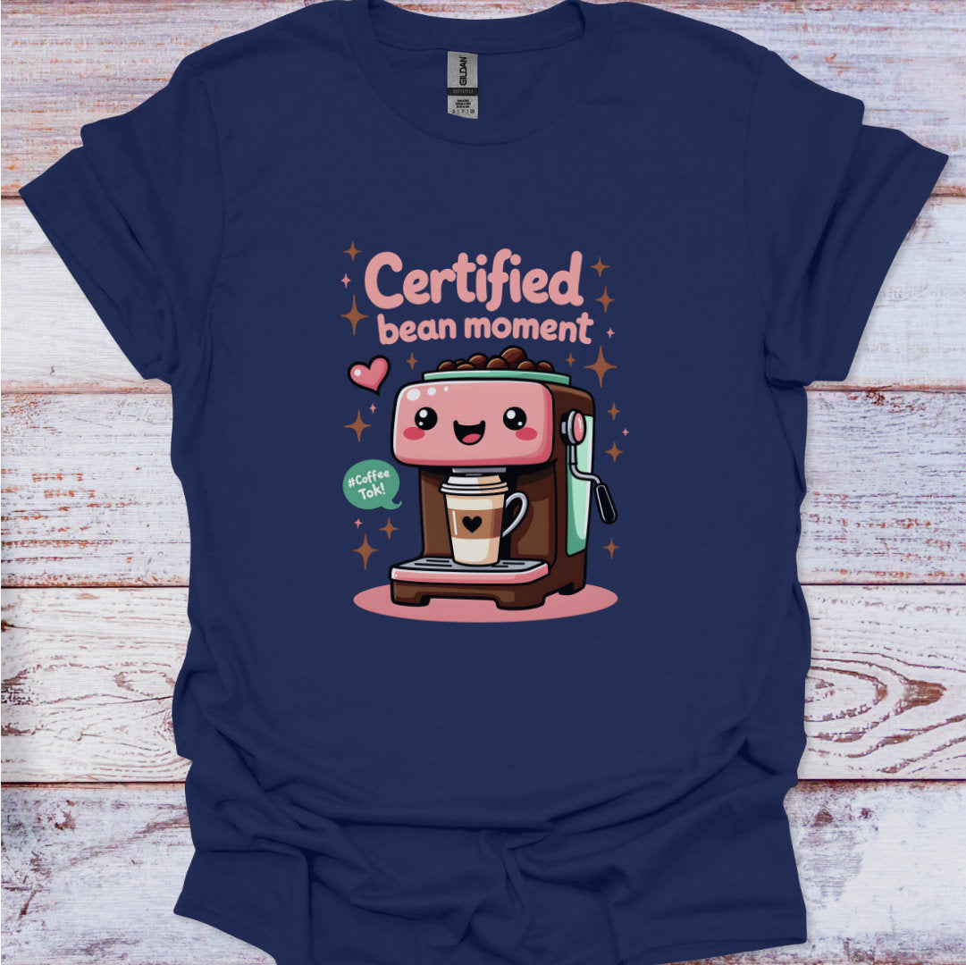 Navy blue t-shirt with a cartoon coffee machine and text 'Certified bean moment' on a wooden surface.
