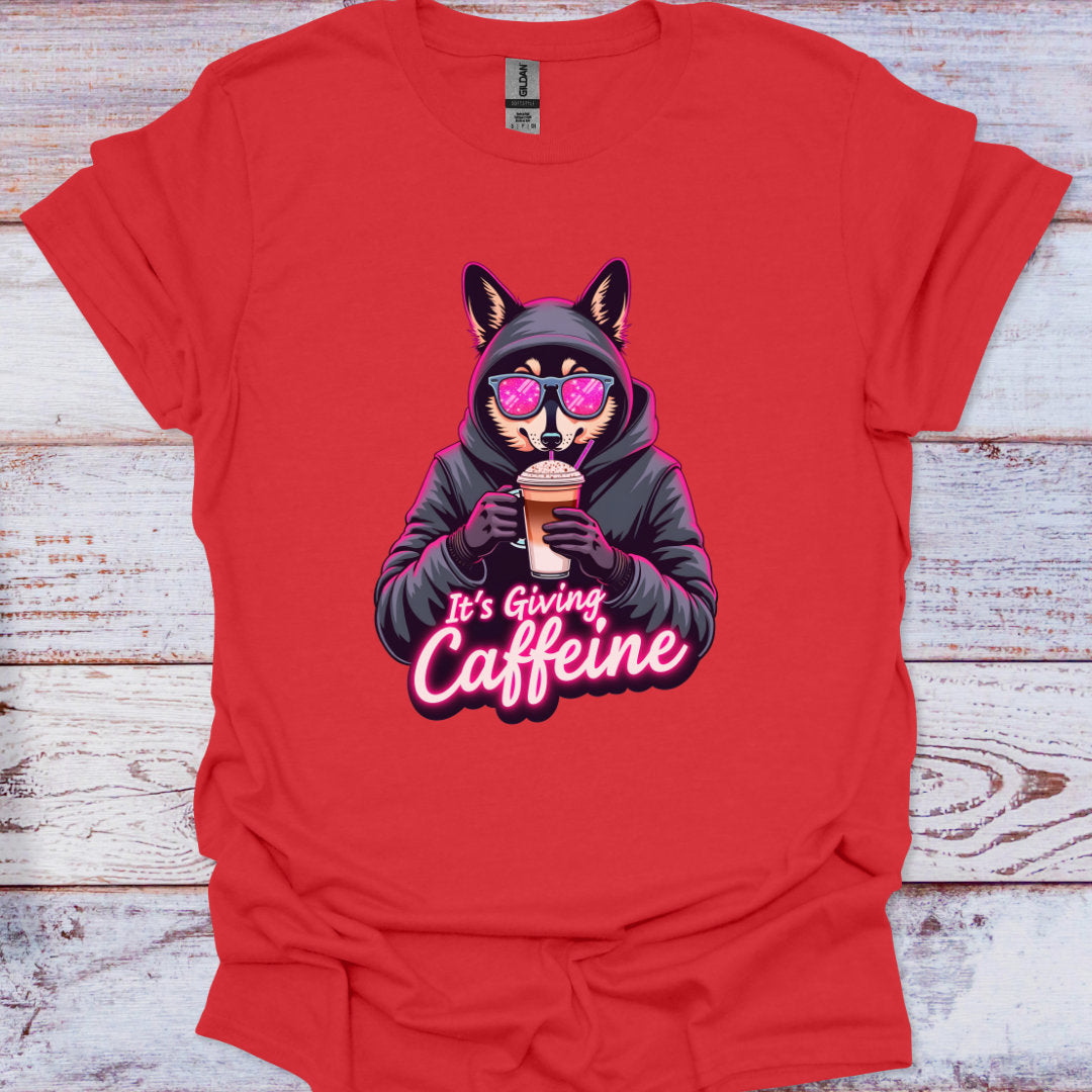 Red t-shirt with a graphic of a dog in a hoodie holding a coffee cup and text 'It's Giving Caffeine' on a wooden surface.