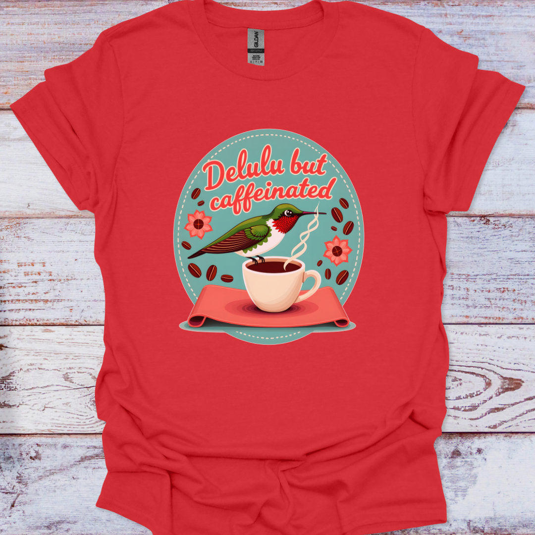Red t-shirt with a graphic of a bird drinking from a coffee cup and text 'Delulu but caffeinated' on a wooden surface.