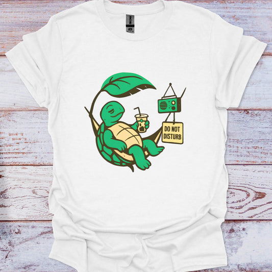 White t-shirt with a green turtle graphic and 'Do Not Disturb' sign on a wooden surface