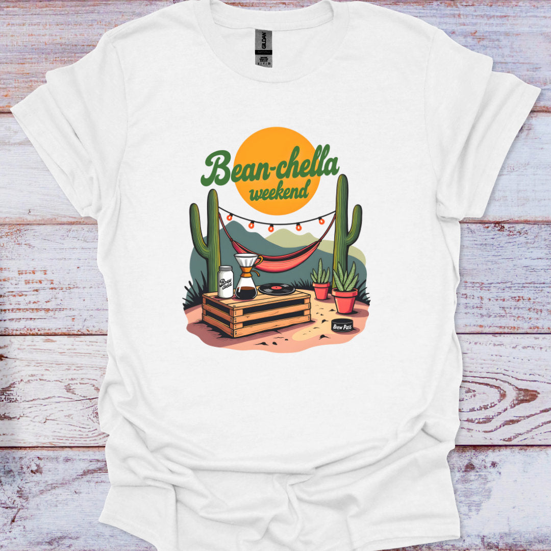 White t-shirt with a graphic design featuring cacti, a hammock, and 'Bean-chella weekend' text on a wooden surface.