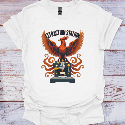 White t-shirt with a graphic design of an mythic phoenix bird and coffee machine on a wooden surface