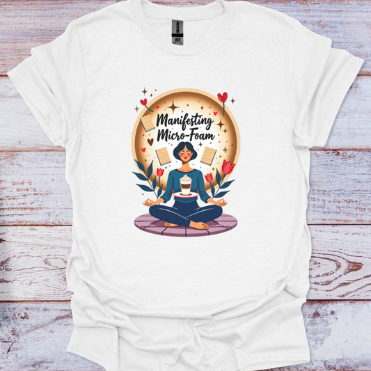 White t-shirt with a graphic design of a person meditating, surrounded by flowers and text, on a wooden surface.