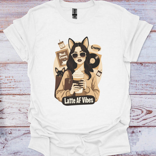 White t-shirt with a graphic design of a woman holding a coffee cup and text 'Latte AF Vibes' on a wooden surface.
