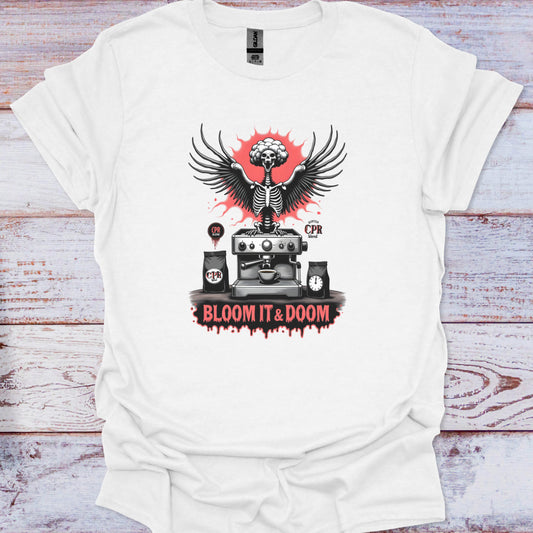 White t-shirt with a graphic design featuring a skeleton, coffee machine, and text on a wooden surface.