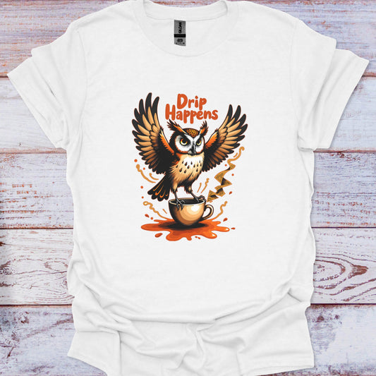 White t-shirt with an owl holding a coffee cup and 'Drip Happens' text on a wooden surface
