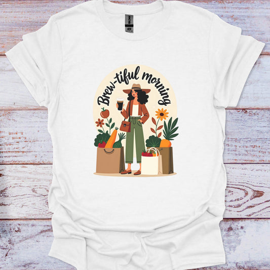 White t-shirt with a graphic of a woman holding a coffee cup and surrounded by groceries and plants, with 'Brew-iful morning' text.