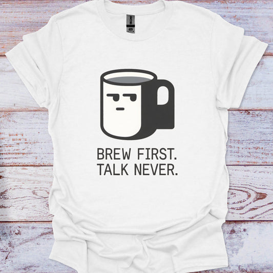 White t-shirt with a coffee mug graphic and text 'Brew First. Talk Never.' on a wooden surface.