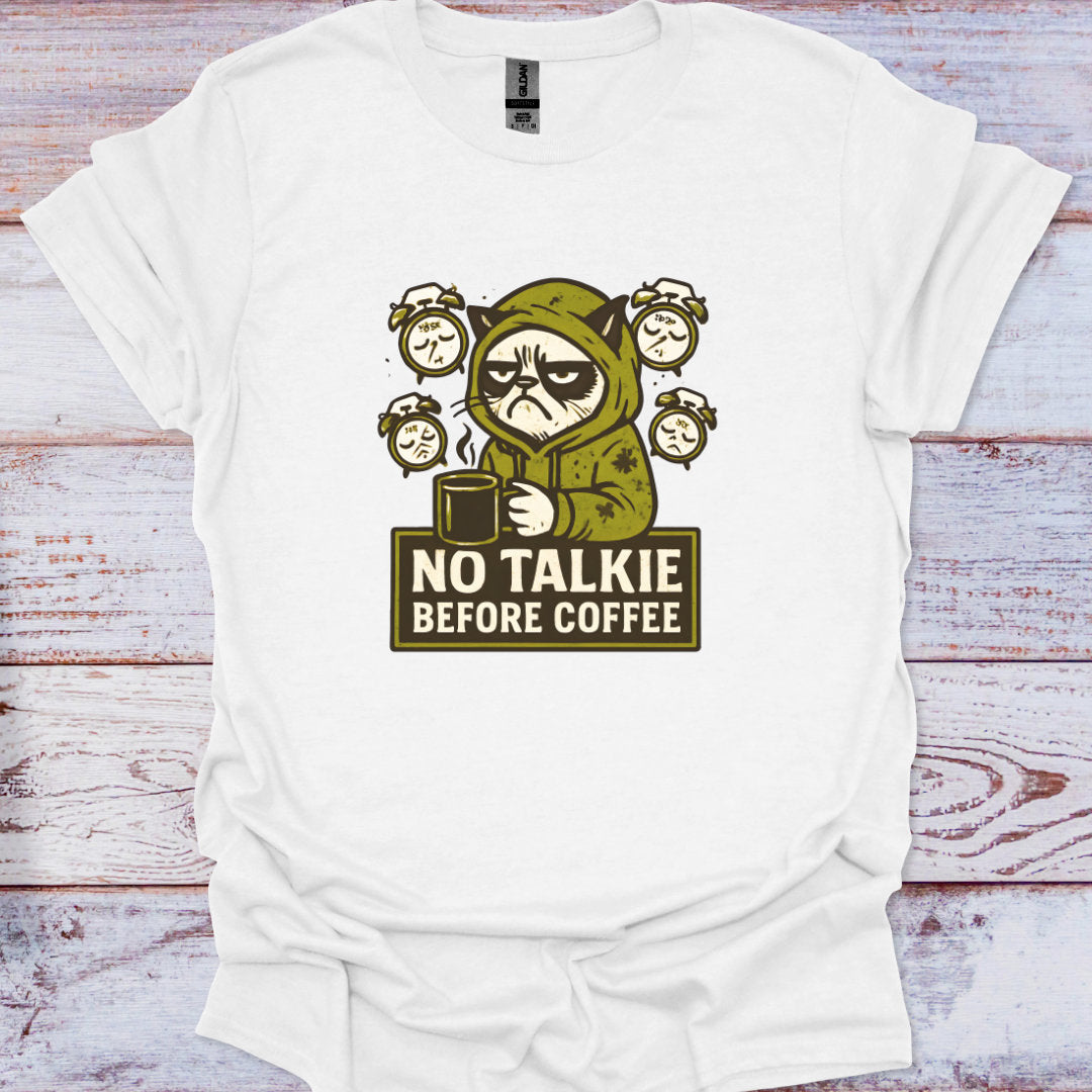 White t-shirt with a graphic of a character holding a coffee cup and text 'No Talkie Before Coffee' on a wooden surface.