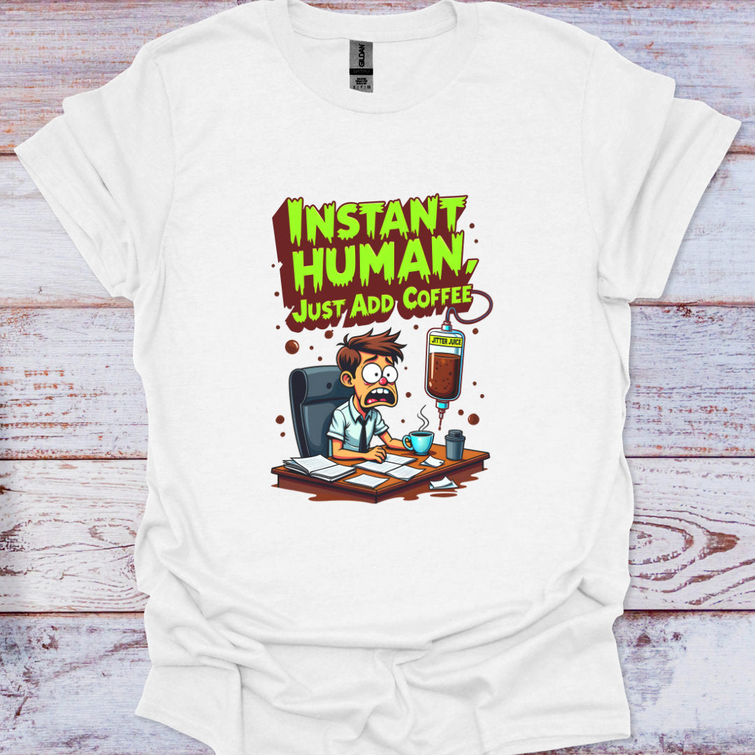White t-shirt with a cartoon design and text 'Instant Human, Just Add Coffee' on a wooden surface.